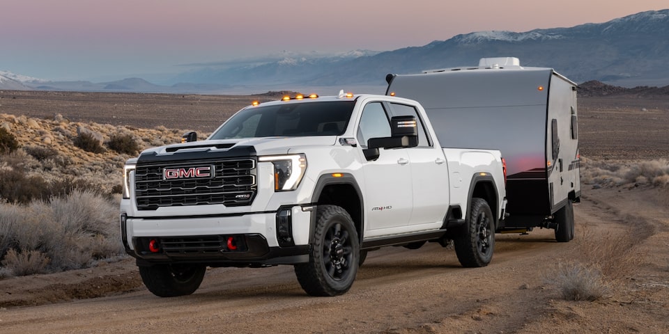 The Sierra HD AT4 Towing a Camper with Ease While Driving Off-Road in the Desert with Mountains in the Distance