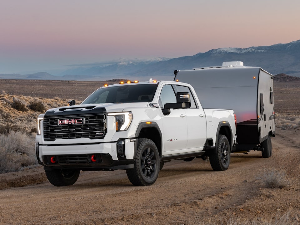 Front Three-Quarters View of a 2024 GMC Sierra HD 2500 AT4 Off-Road Work Truck Hauling a Trailer at Dusk