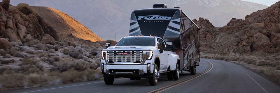 The Sierra HD Denali Driving on a Bend While Towing a Massive Camper in the Desert