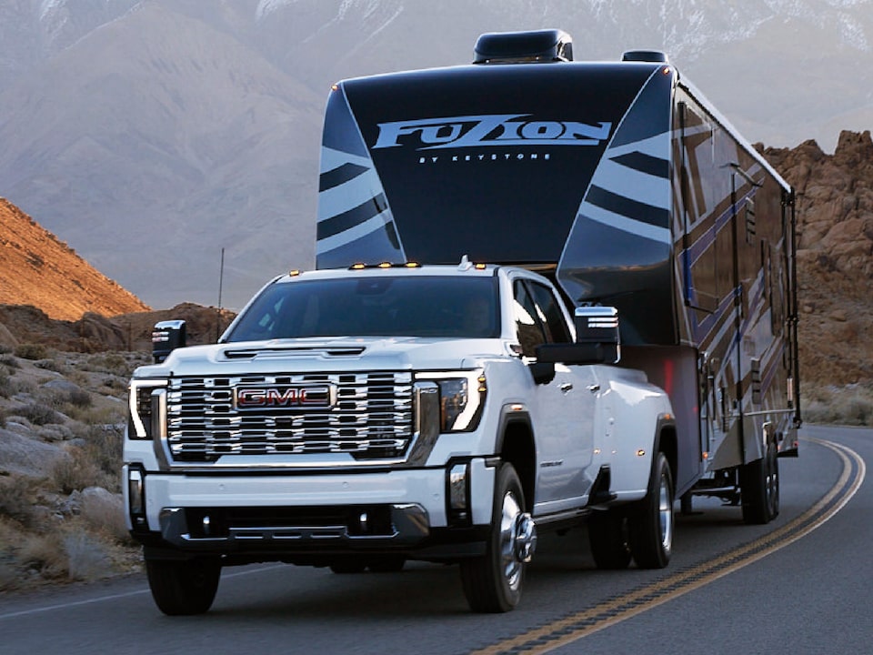 A White GMC Sierra HD Pro Driving On-Road Towing a Trailer