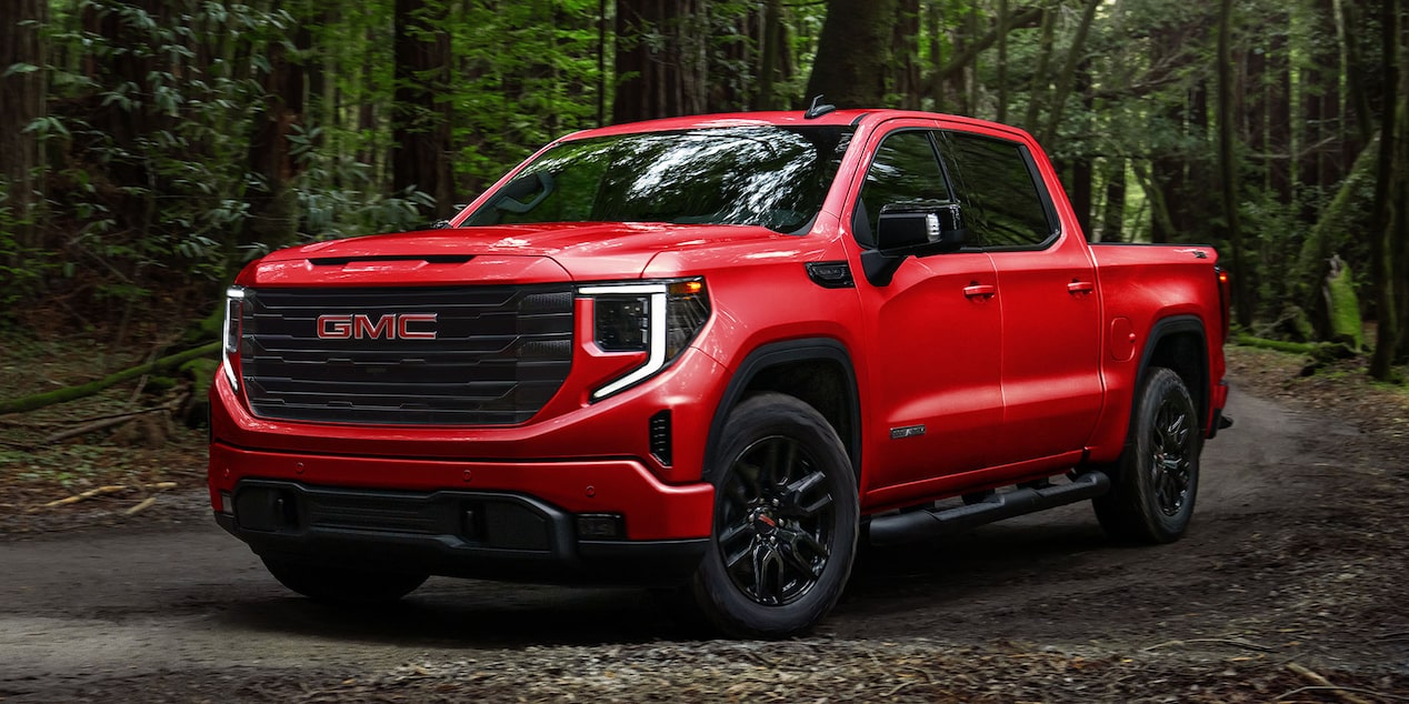 Red with black accents GMC Sierra parked in a forested area