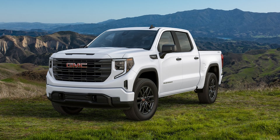 A White 2024 GMC Sierra 1500 SLE Parked on Grassy Hills with Mountains in the Distance