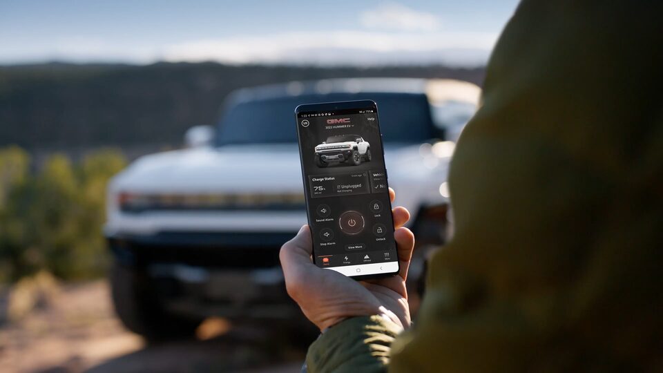 Close-Up View of a Person Utilizing the myGMC Mobile App with the 2025 Hummer EV is Parked in Background
