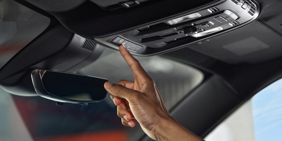 A Man Sitting in the Driver Seat of the GMC Acadia Pressing the Vehicle's OnStar Button