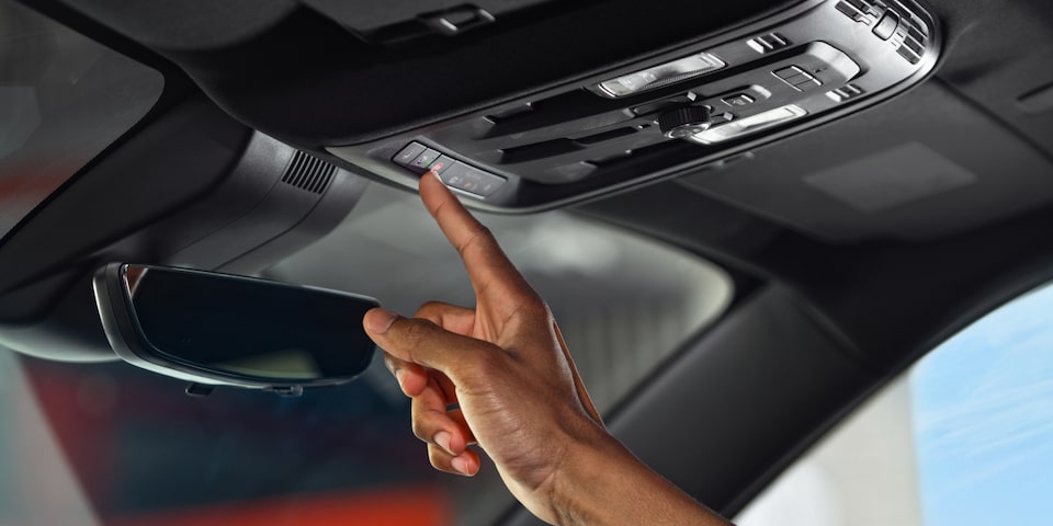 A Man Sitting in the Driver Seat of the GMC Acadia Pressing the Vehicle's OnStar Button