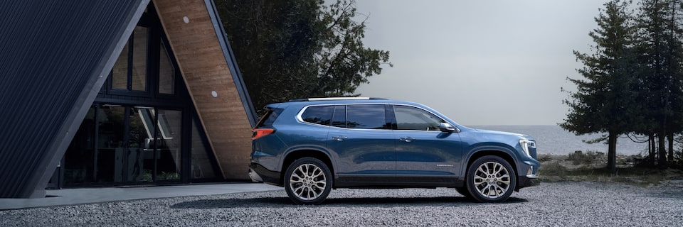 Profile View of a Blue GMC Acadia Parked Next to a Beautiful Cabin in the Woods