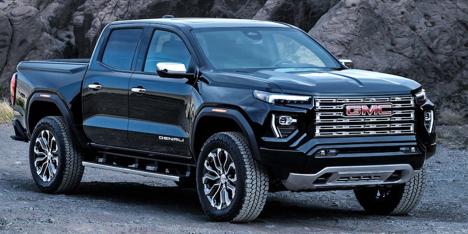 Rear Three-quarter View of a Black 2025 GMC Canyon Parked Near a Modern Mountain Cabin