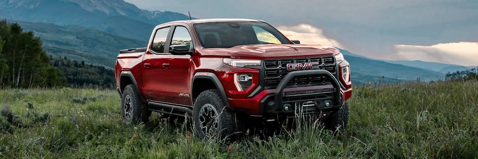 Three-quarter View of a Red 2025 GMC Canyon AT4 Parked in a Grassy Field