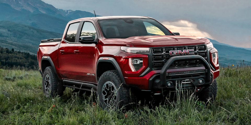 Three-quarter View of a Red 2025 GMC Canyon AT4 Parked in a Grassy Field