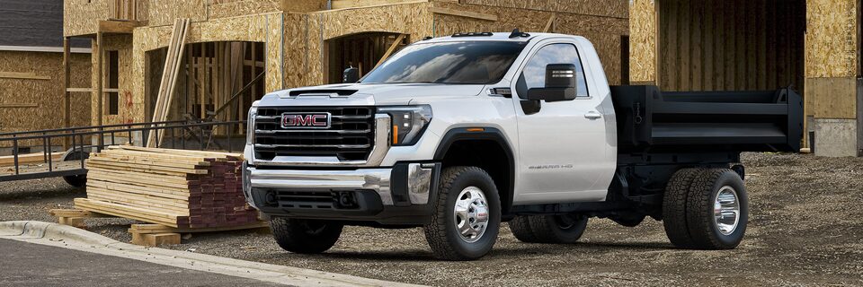 Wide Front Three-Quarters View of a 2025 GMC Sierra HD Chassis Cab Truck Parked in Front of a House Under Construction