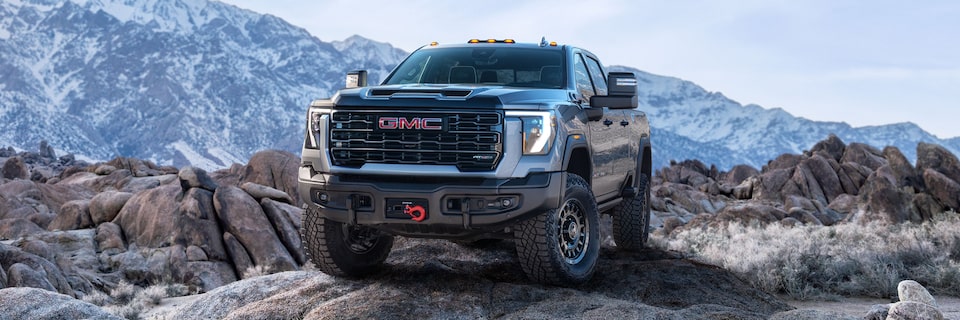 Wide Front Three-Quarters View of a 2025 GMC Sierra HD AT4 Truck Parked in Front of Snow-Covered Mountains