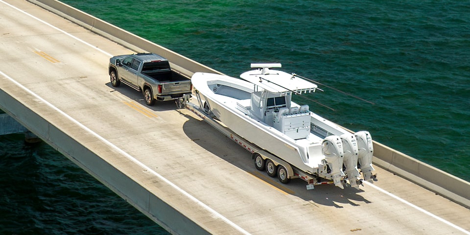 Wide Rear Three-Quarters Birdseye View of a 2025 GMC Sierra HD Hauling a Boat on an Open Road Near a Lake