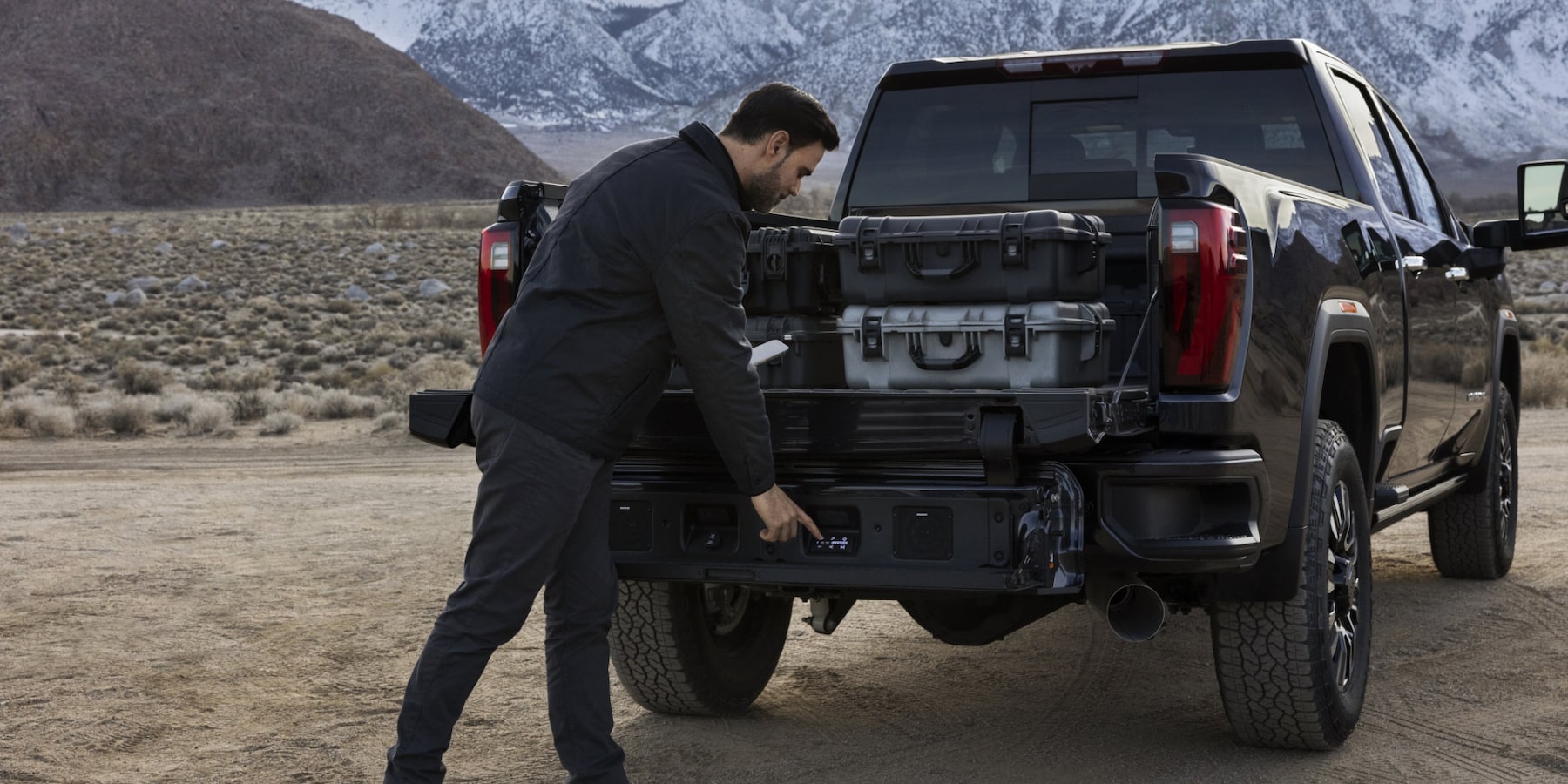 Man using the GMC Sierra 3500 Six-Function Multipro Tailgate to load large pelican cases in to the extended cab truck bed