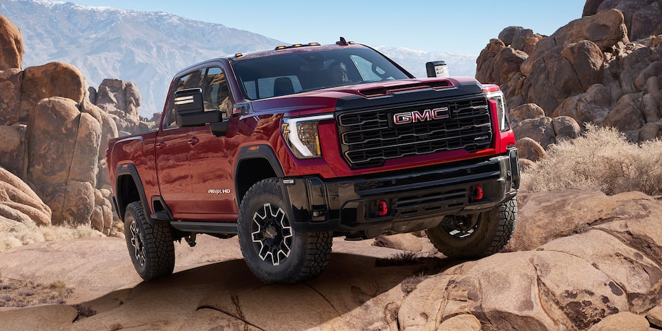 Front Three-Quarters View of a 2025 GMC Sierra HD AT4 Parked on Rocky Ground Surrounded by Mountains