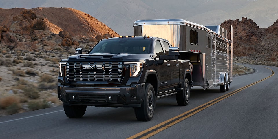 Front Three-Quarters View of a 2025 GMC Sierra HD Denali Luxury Truck Hauling a Trailer Through the Mountains
