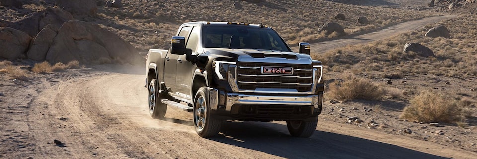 Wide Front Three-Quarters View of a 2025 GMC Sierra 2500 HD Truck Driving Through the Desert