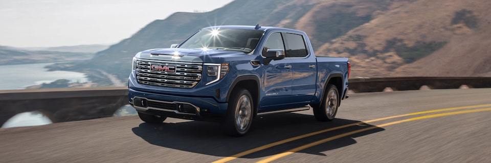 2025 GMC Sierra 1500 Driving Down a Winding Road with Mountains in the Background