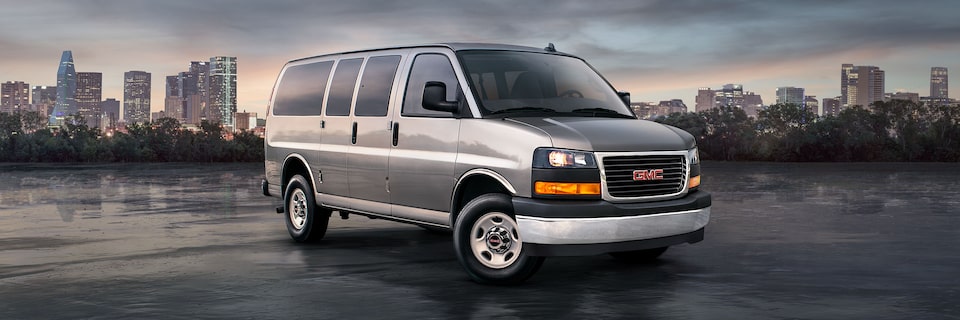 Wide Front Three-Quarters View of a 2025 GMC Savana Passenger Van with a City in the Background