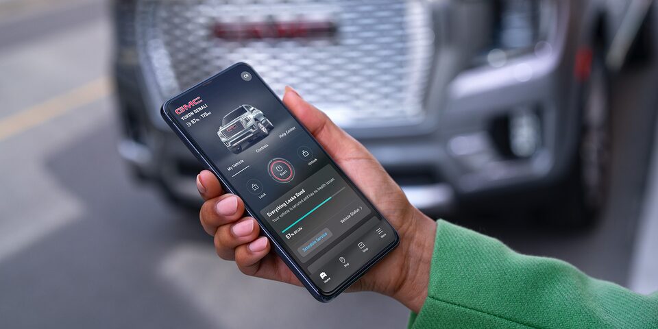 A Person Holding a Smartphone with the myGMC App Open Showing Vehicle Health and Specs