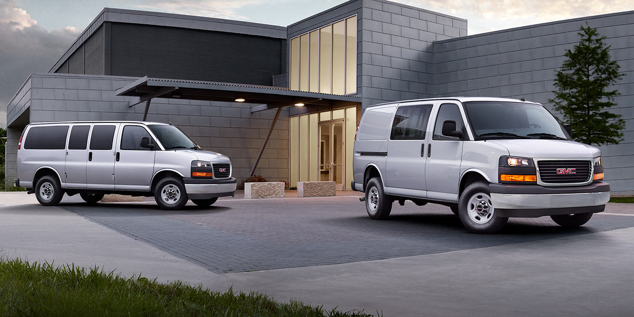 Two Silver 2026 GMC Savana Vans, a Passenger Van and a Cargo Van, Parked outside a Modern Building