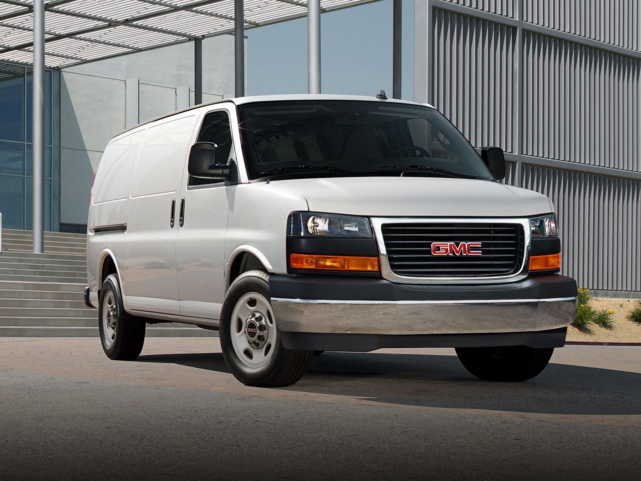 A White 2026 GMC Savana Van Parked on Asphalt in Front of a Modern Building with Concrete Stairs