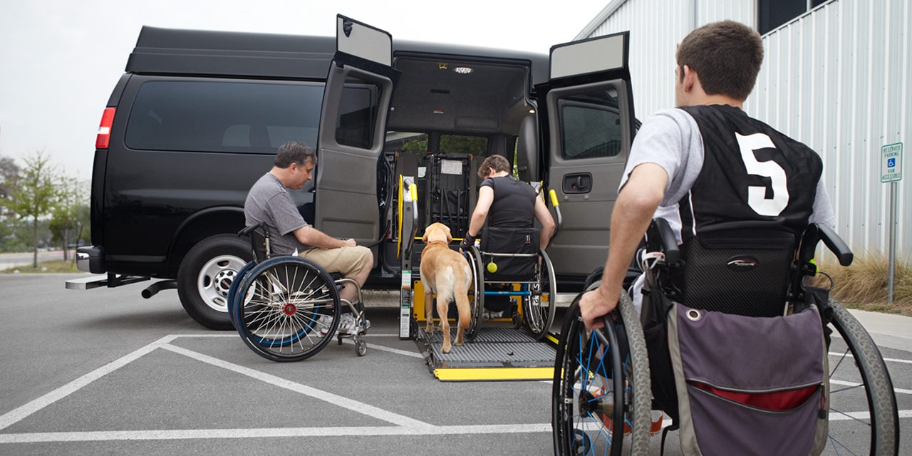 A Person in a Wheelchair Using the Lift Feature on the 2026 GMC Savana Passenger Van with a Dog by His Side