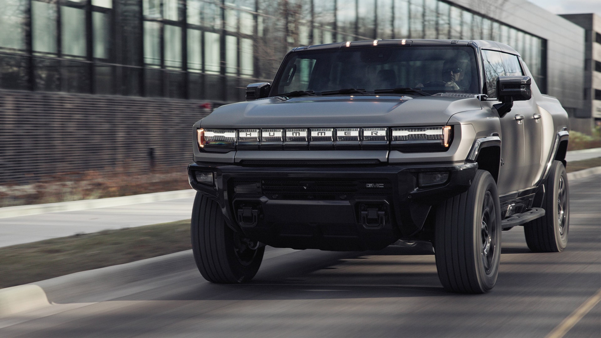 The 2026 GMC HUMMER EV Pickup Truck Driving Past a Business Building