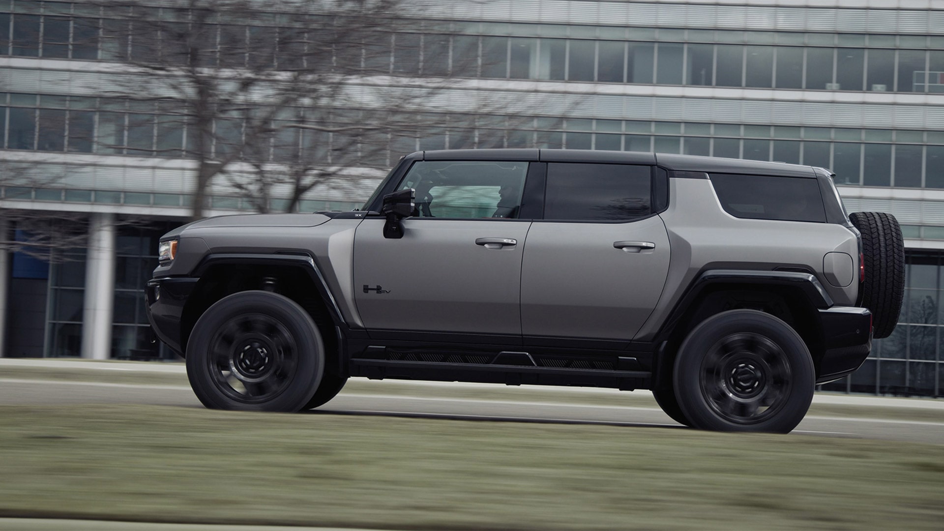Blurry Driver Side View of the 2026 GMC HUMMER EV SUV Driving Past a Building