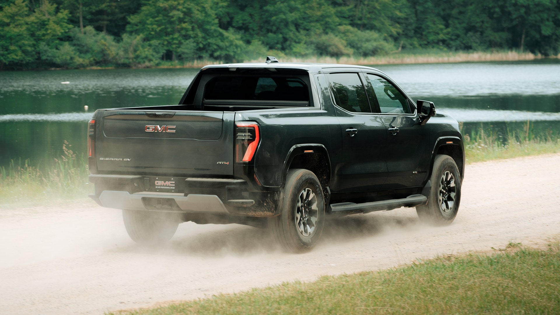 Rear View of the 2026 GMC Sierra EV AT4 Pickup Truck Driving and Kicking up Dust