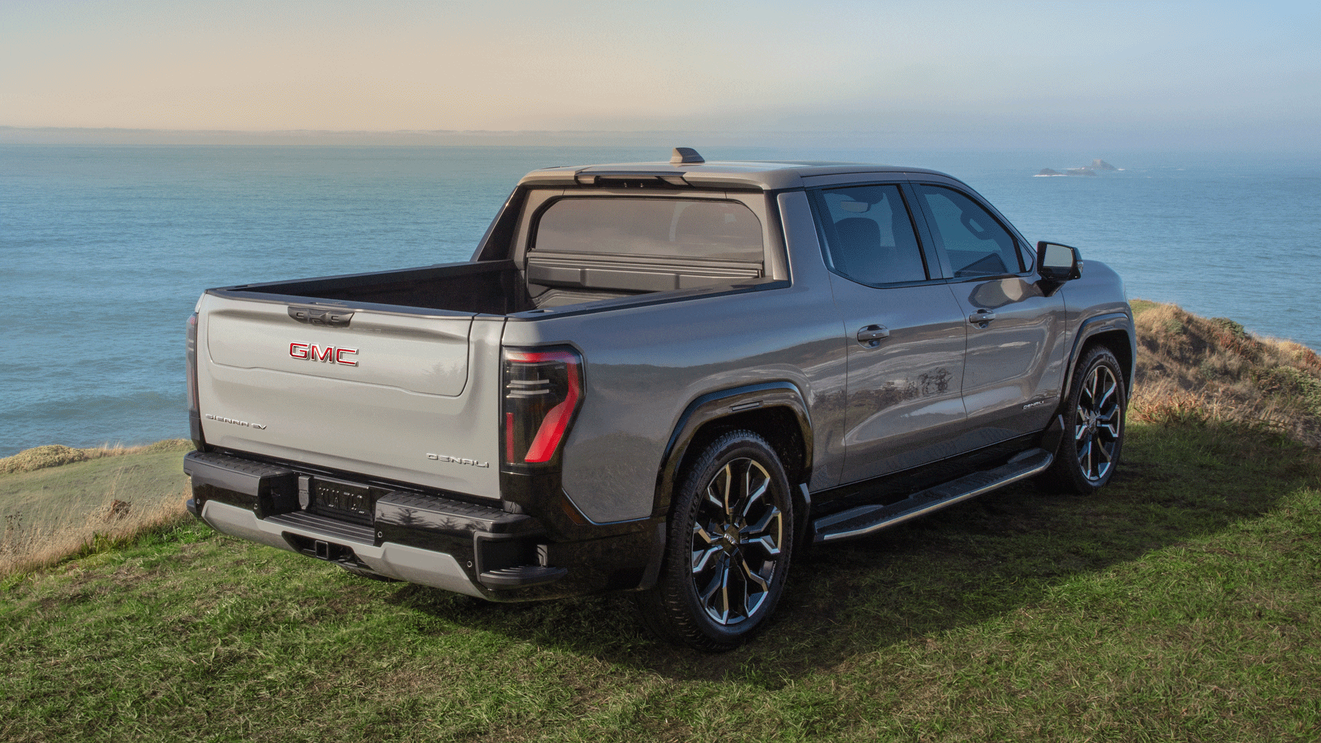The 2026 GMC Sierra EV AT4 Parked on a Grassy Cliff Over looking a Body of Water with the Multipro Tailgate Open