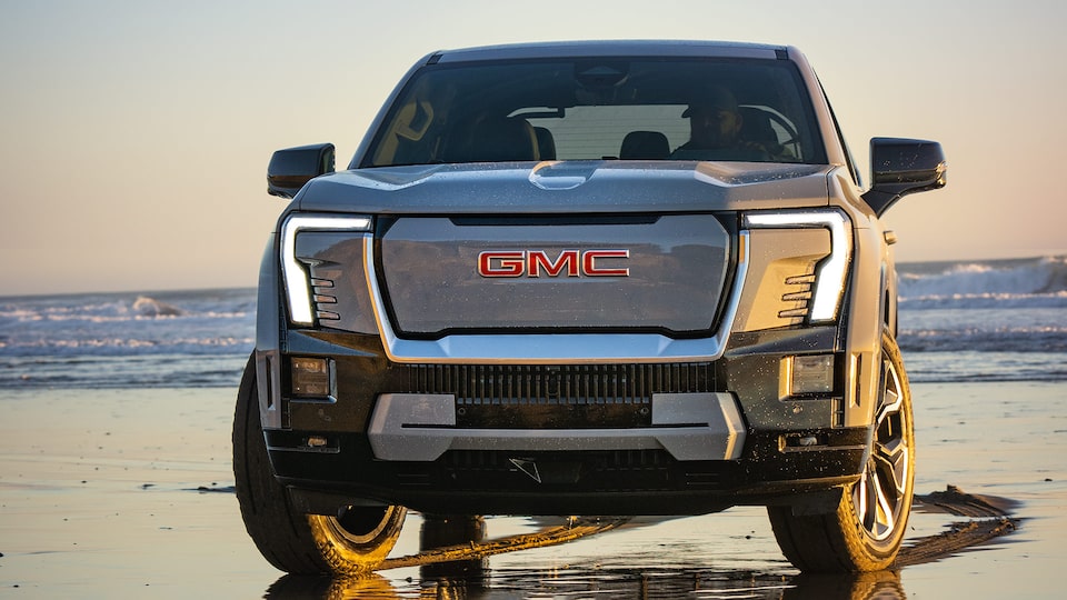 Front View of a 2026 GMC Sierra EV Pickup Truck Parked on a Beach Gleaming During a Beautiful Sunset