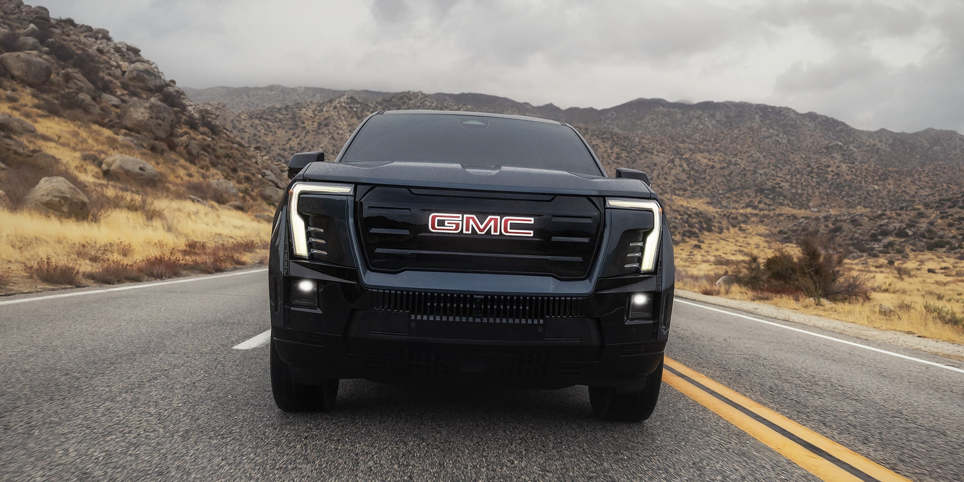 Front View of the 2026 GMC Sierra EV Elevation Driving Down the Open Road with a Mountain Range in the Distance
