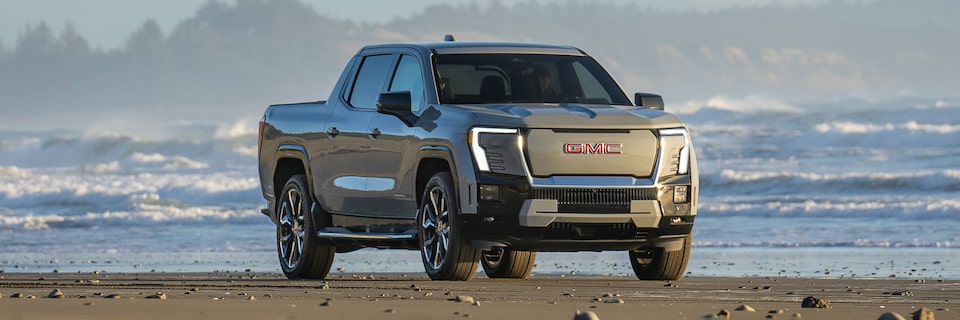 Three-quarters Passenger View of a 2026 GMC Sierra EV Pickup Truck Parked on a Beach Gleaming Under the Sun