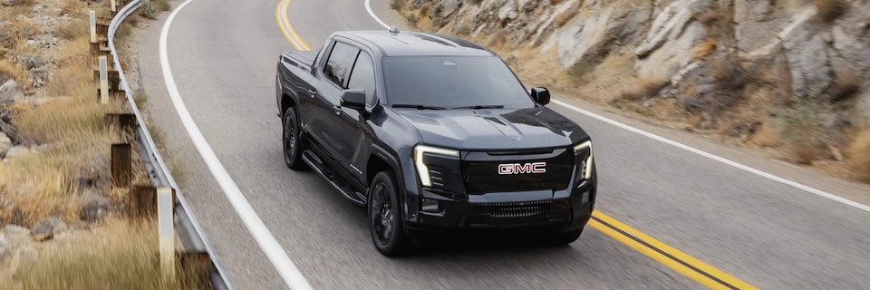 Three-quarters Passenger Side View of a Black 2026 GMC Sierra EV Driving Through a Mountain Road