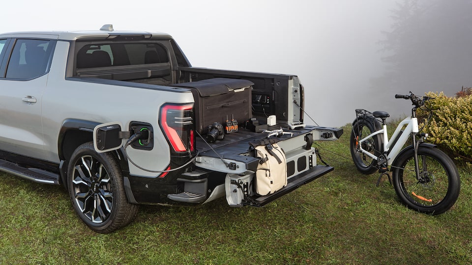 The 2026 GMC Sierra EV Charging Through a Portable Charger in the Bed and the Multipro Tailgate Being Utilized
