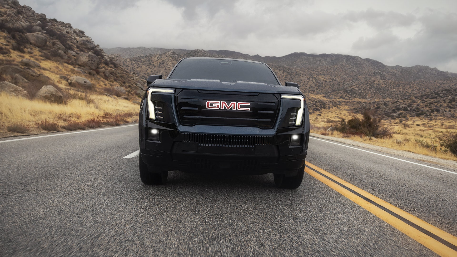 A Low Front View of the 2026 GMC Sierra EV Driving Through a Mountain Road