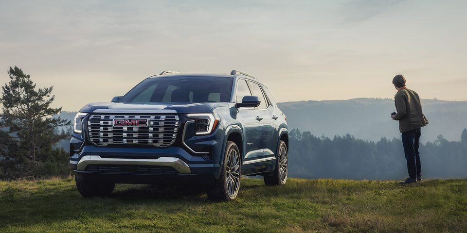 Front Three-Quarters View of a 2026 GMC Terrain Denali Parked at the Edge of a Cliff with the Driver Standing Next to the Terrain Taking in the Scenic View