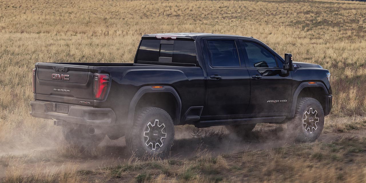 Rear Three-quarter View of a Black 2026 GMC Sierra HD Heavy Duty Truck Off-roading and Kicking Up Dirt