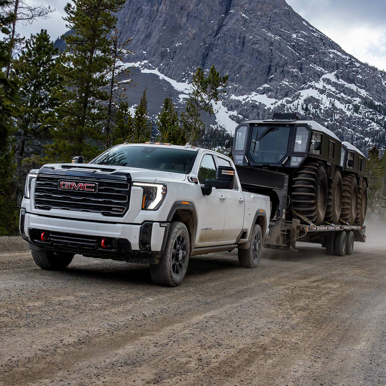 The 2026 GMC Sierra HD Heavy Duty Truck Pulling a Trailer Down a Dirt Road Lined with Pine Trees
