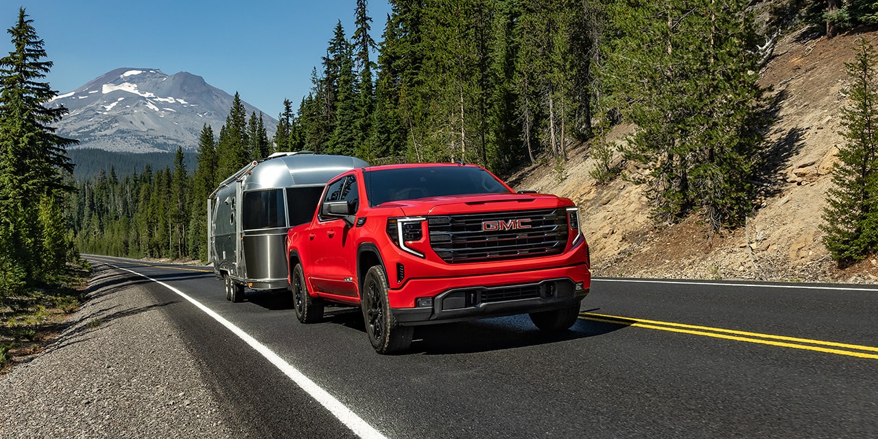 A Red GMC Sierra AT4X Truck Towing a Silver Travel Trailer on a Highway