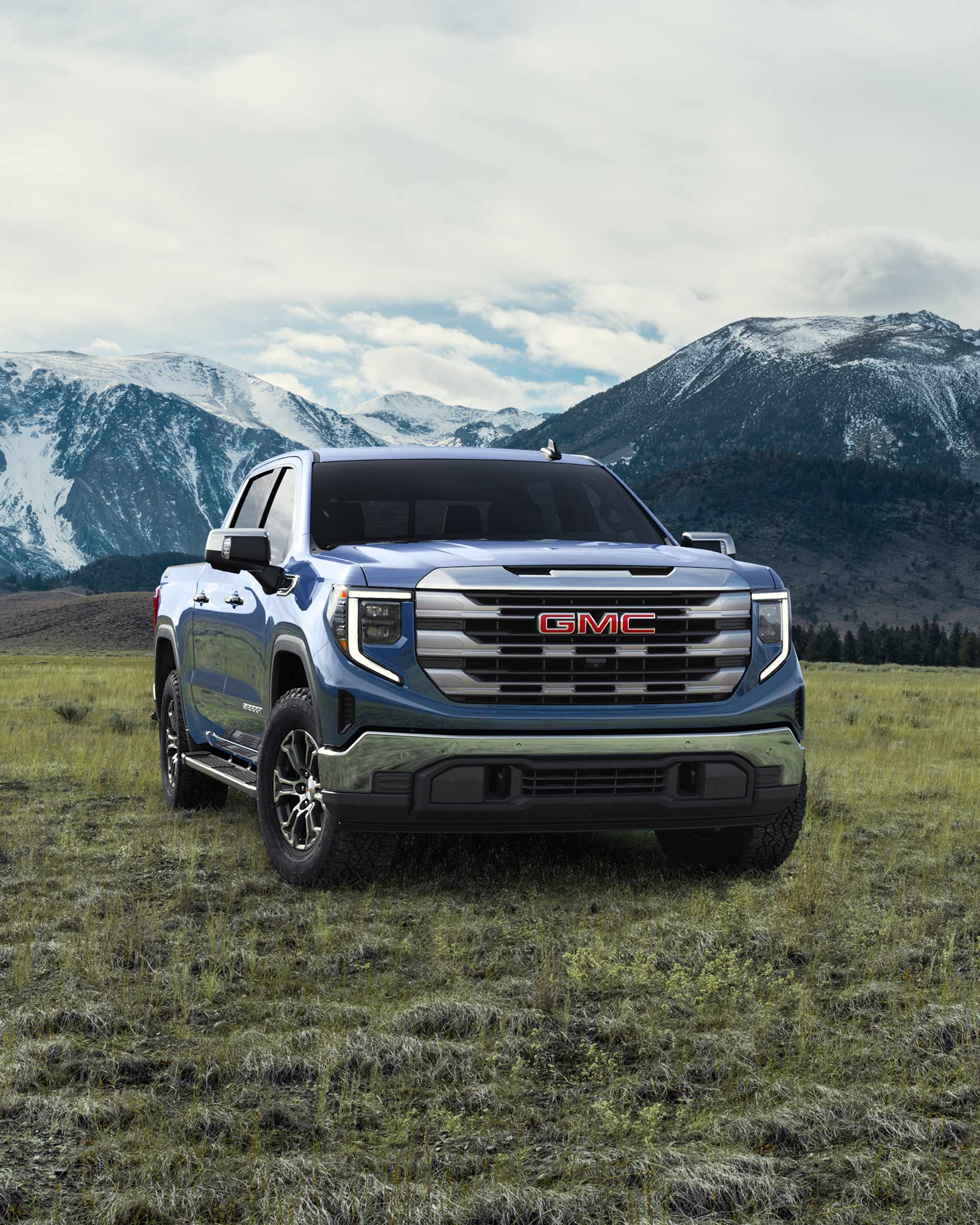 A Blue GMC Sierra Truck in a Grassy Field with Snowy Mountains in the Background