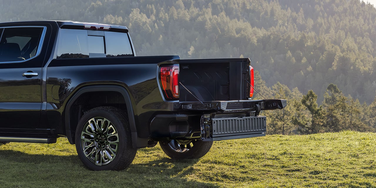 A Black GMC Sierra Truck with its MultiPro Tailgate Lowered and Extended on a Grassy Hill