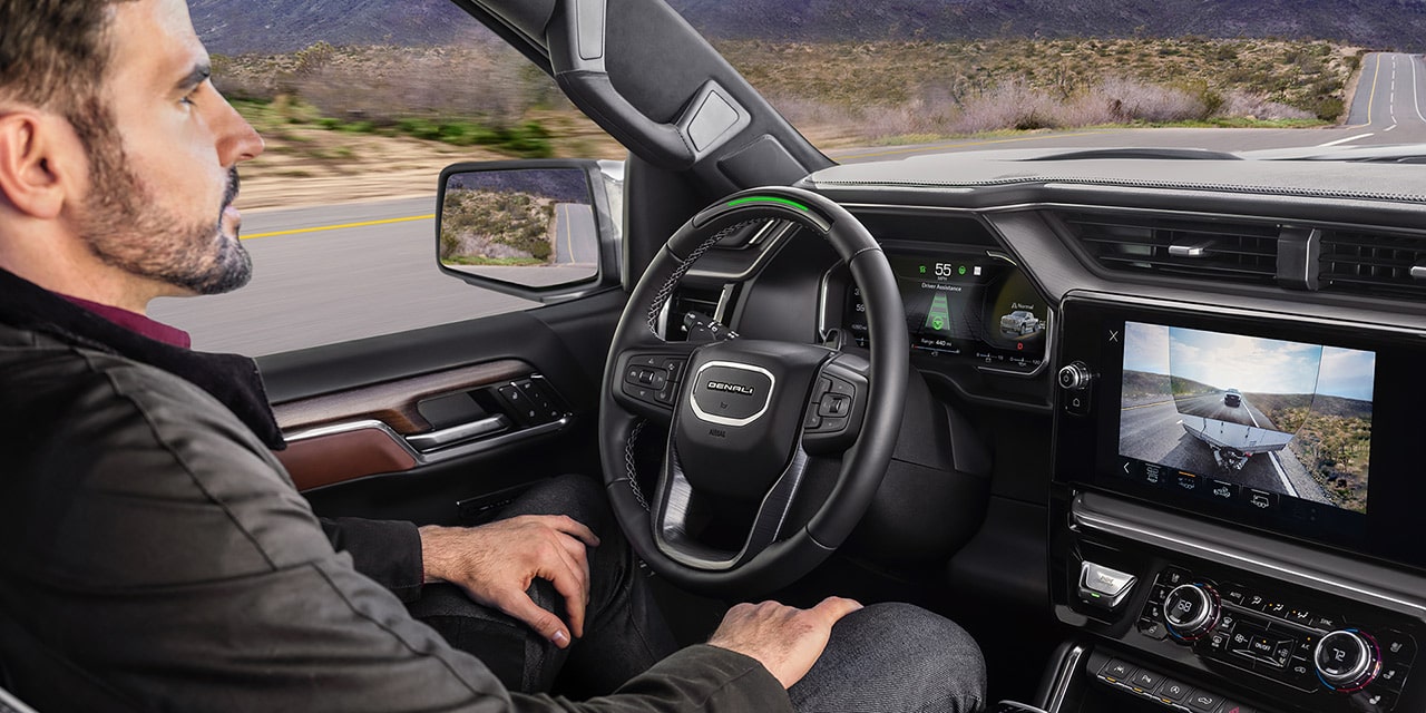 A Man Driving a GMC Sierra Truck, with a View of the Denali Super Cruise Display Showing Trailering