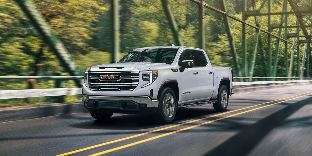 Front Three-Quarters View of the GMC Sierra 1500 Pickup Truck Driving Over a Bridge as the Sun Shines