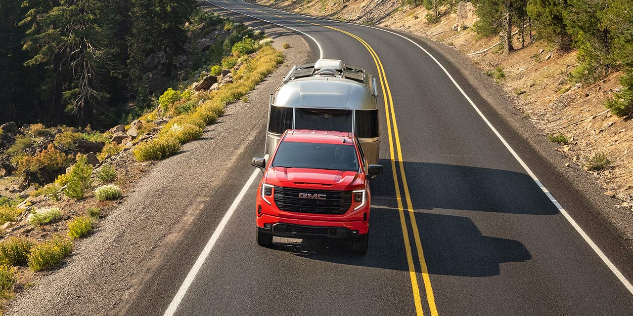 Birds-eye View of the 2026 GMC Sierra 1500 Pickup Truck Towing a Trailer Down a Road Lined with Trees