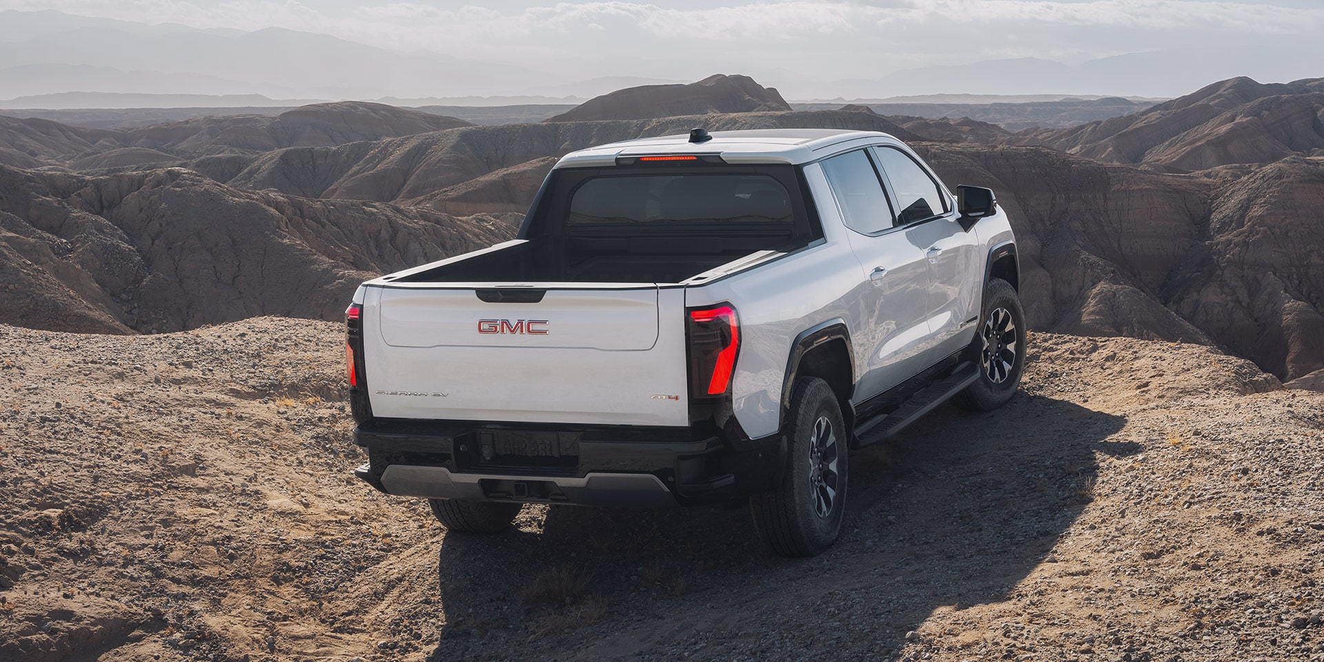 The rear view of a white GMC Sierra EV AT4 Parked on a Desert Landscape