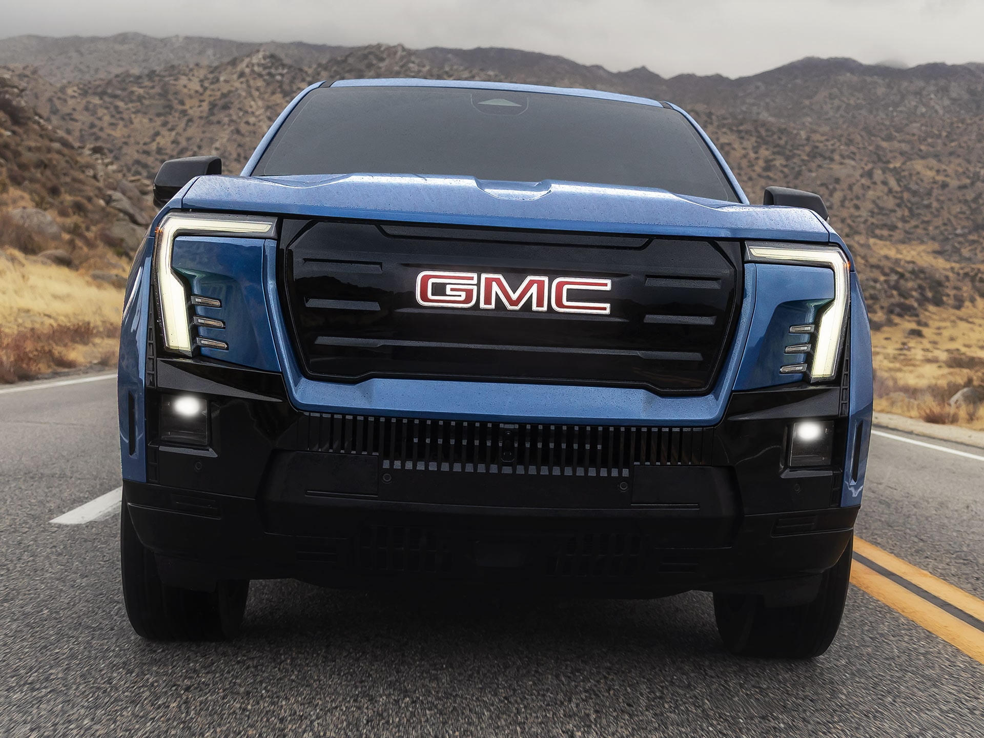 The Front Exterior Styling of a Bold Blue GMC Sierra EV Driving on a Road
