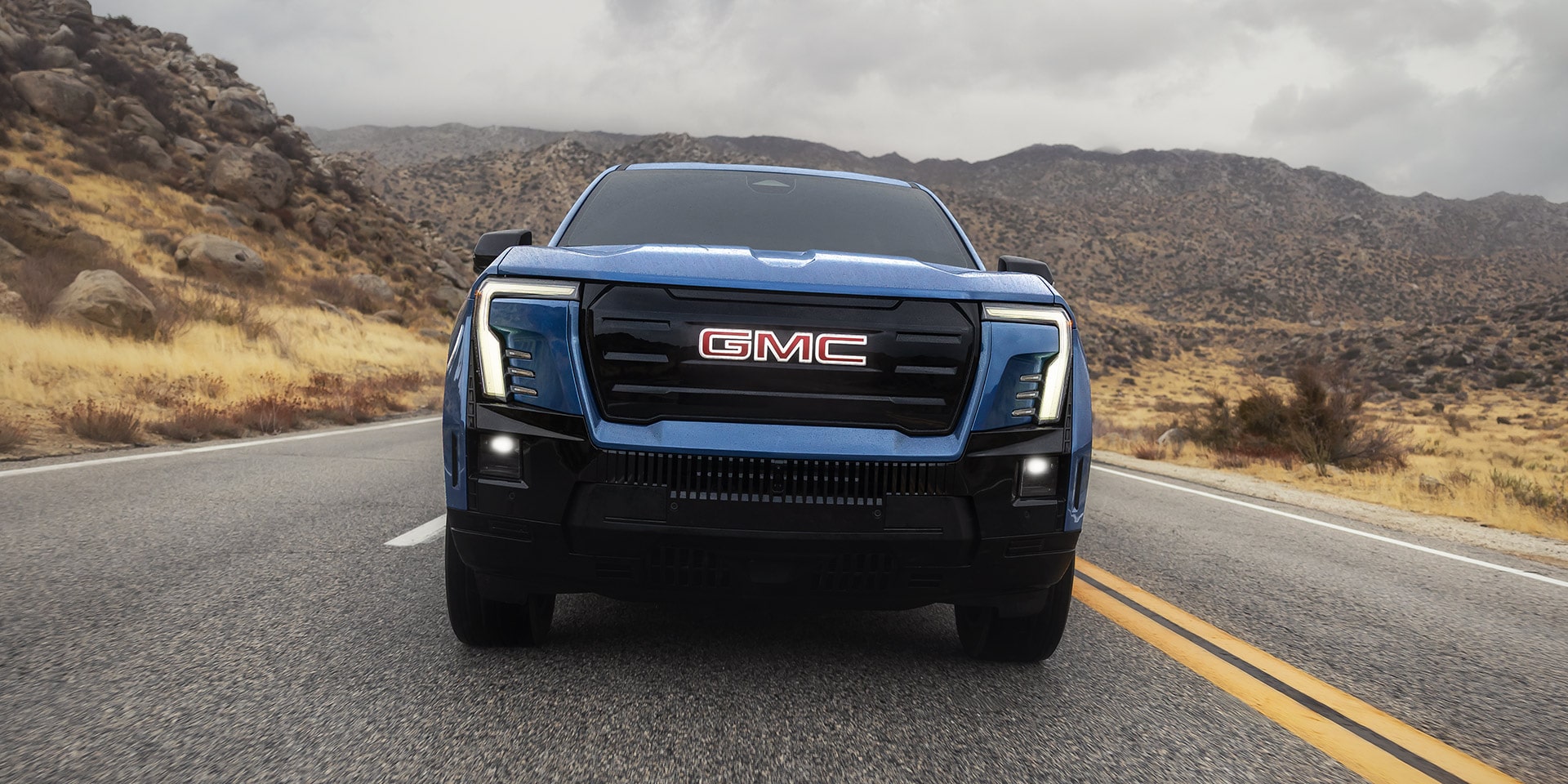 The Front Exterior Styling of a Bold Blue GMC Sierra EV Driving on a Road