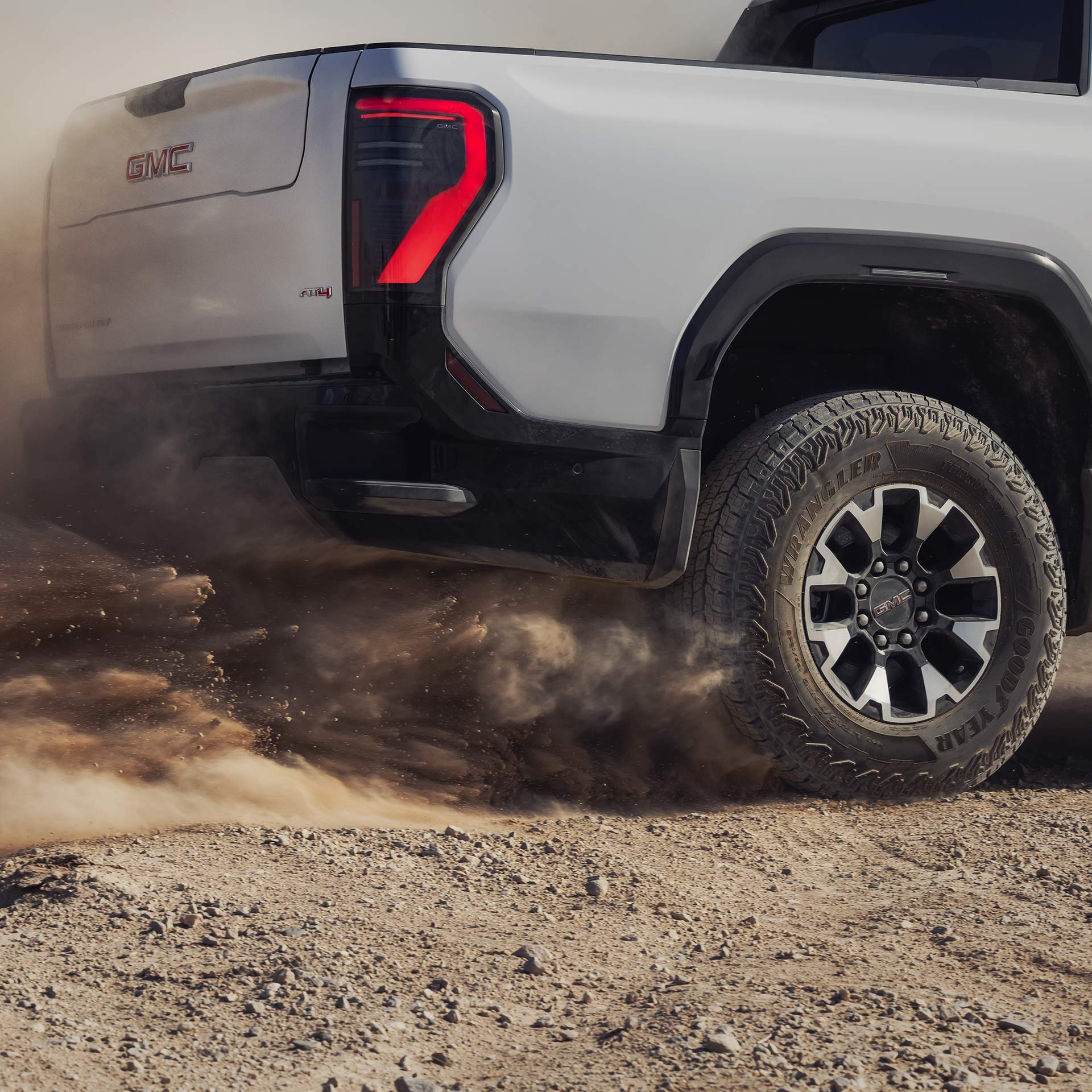 A Close Up View of the Rear Rugged Wheels on a GMC Sierra EV Truck Kicking Up Dust