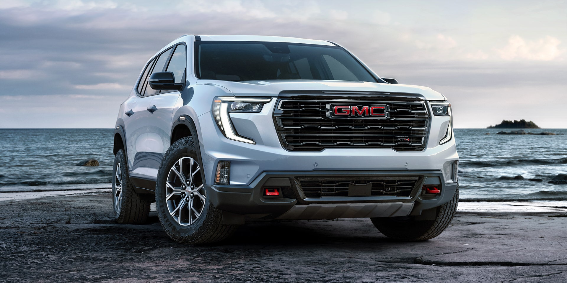 White GMC SUV With the GMC Logo on the Grille Parked on a Rocky Beach Beside the Ocean